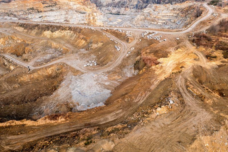 Na zdjęciu widać potężne, skalne ściany kamieniołomu w Strzelinie, z których wydobywa się granit, otoczone przez naturalną roślinność i malownicze jezioro w wykopach.