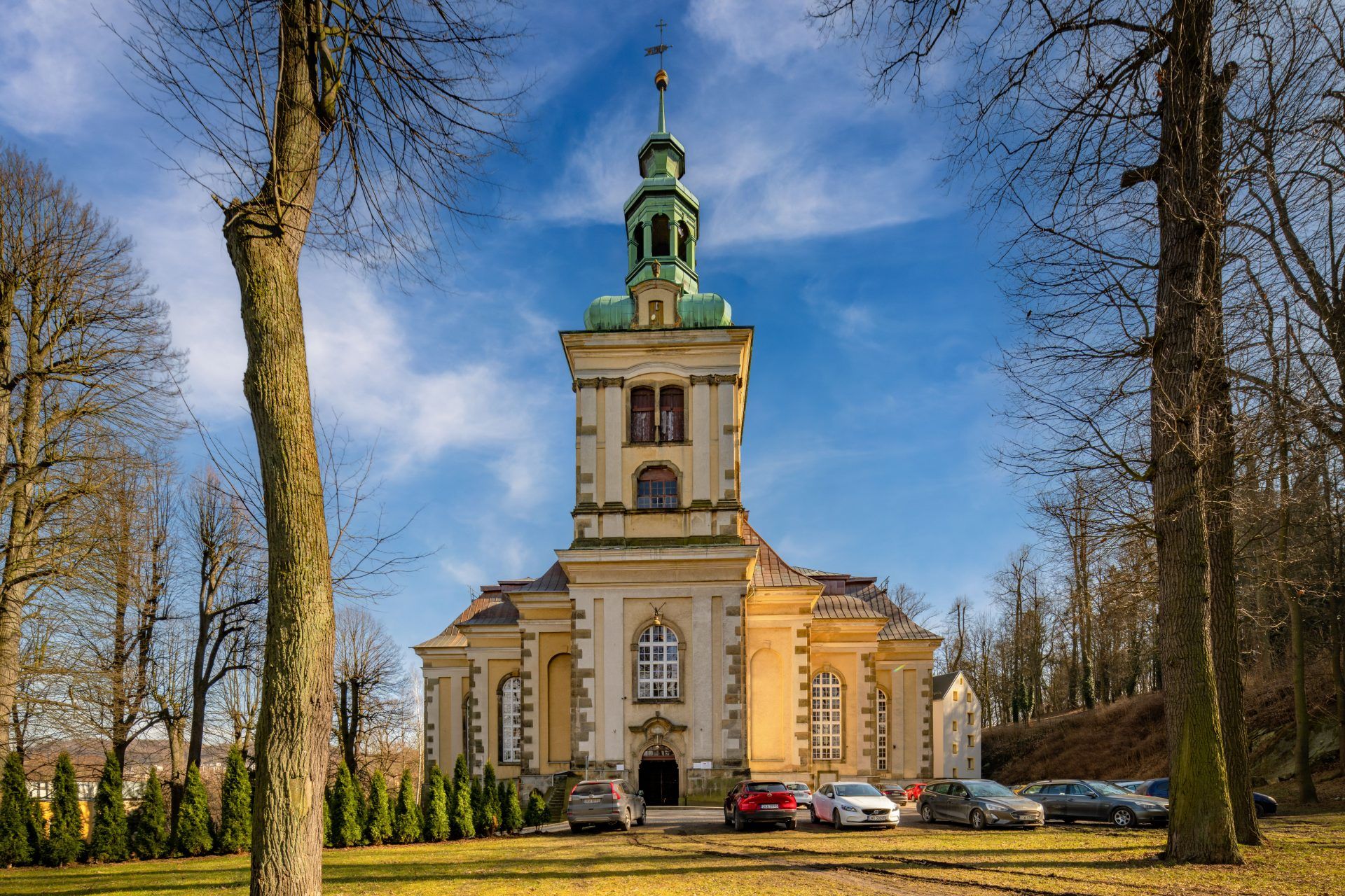Na zdjęciu widać okazały Kościół Łaski w Kamiennej Górze – barokową budowlę o jasnej elewacji, wysokim dachu i smukłej wieży górującej nad otaczającym ją parkiem.
