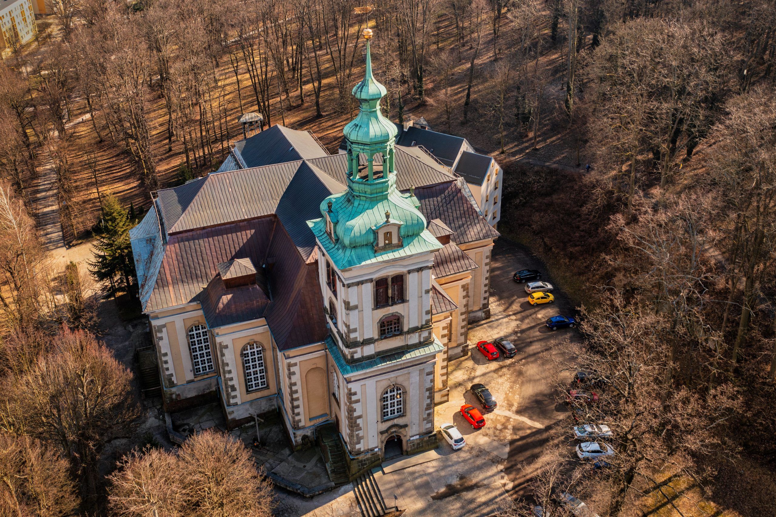 Na zdjęciu widać okazały Kościół Łaski w Kamiennej Górze – barokową budowlę o jasnej elewacji, wysokim dachu i smukłej wieży górującej nad otaczającym ją parkiem.
