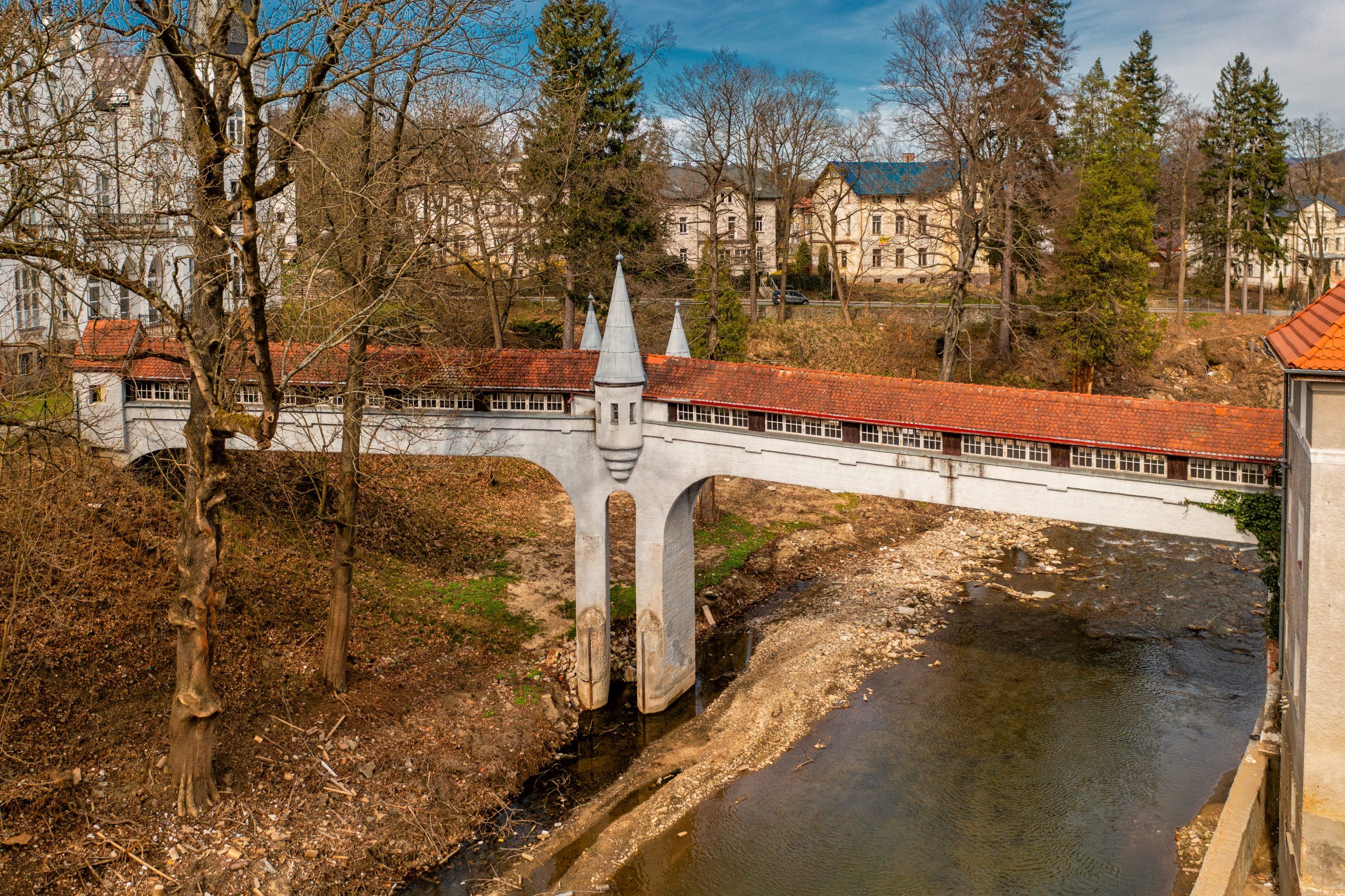 Kryty Most w Lądku-Zdroju to zabytkowa kamienna konstrukcja z łukowym przejściem, przykryta drewnianym dachem, otoczona bujną roślinnością i malowniczym krajobrazem.
