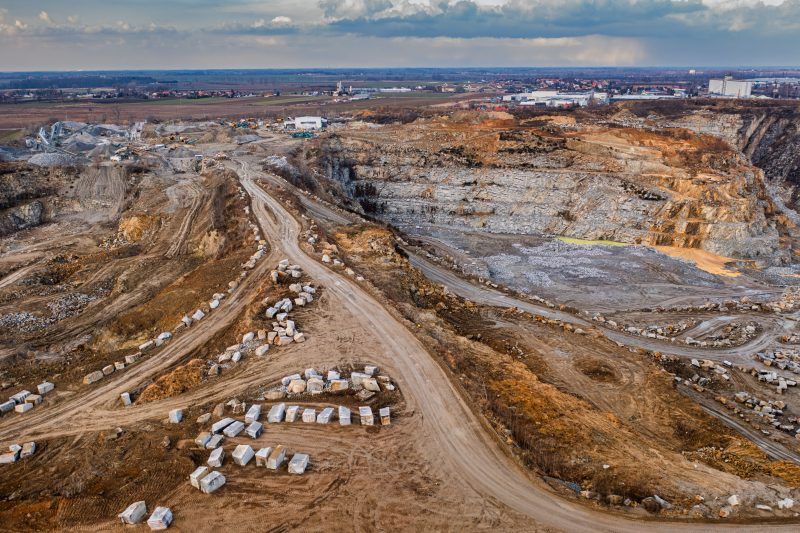 Na zdjęciu widać potężne, skalne ściany kamieniołomu w Strzelinie, z których wydobywa się granit, otoczone przez naturalną roślinność i malownicze jezioro w wykopach.