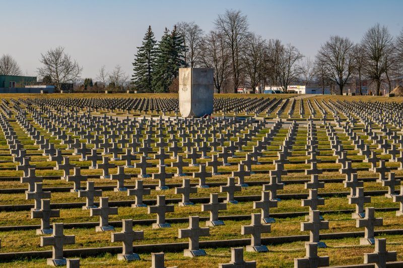 Na zdjęciu widać uporządkowany cmentarz z kamiennymi nagrobkami, otoczony zielenią, z zadbaną przestrzenią upamiętniającą żołnierzy II Armii Wojska Polskiego.