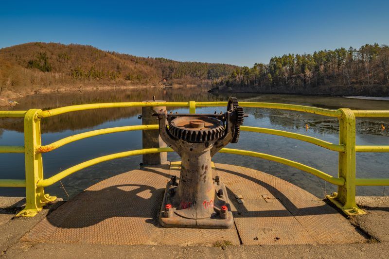 Na zdjęciu widać metalowy mechanizm zębaty przy żółtej barierce, stojący na platformie nad wodą zapory w Pilchowicach.