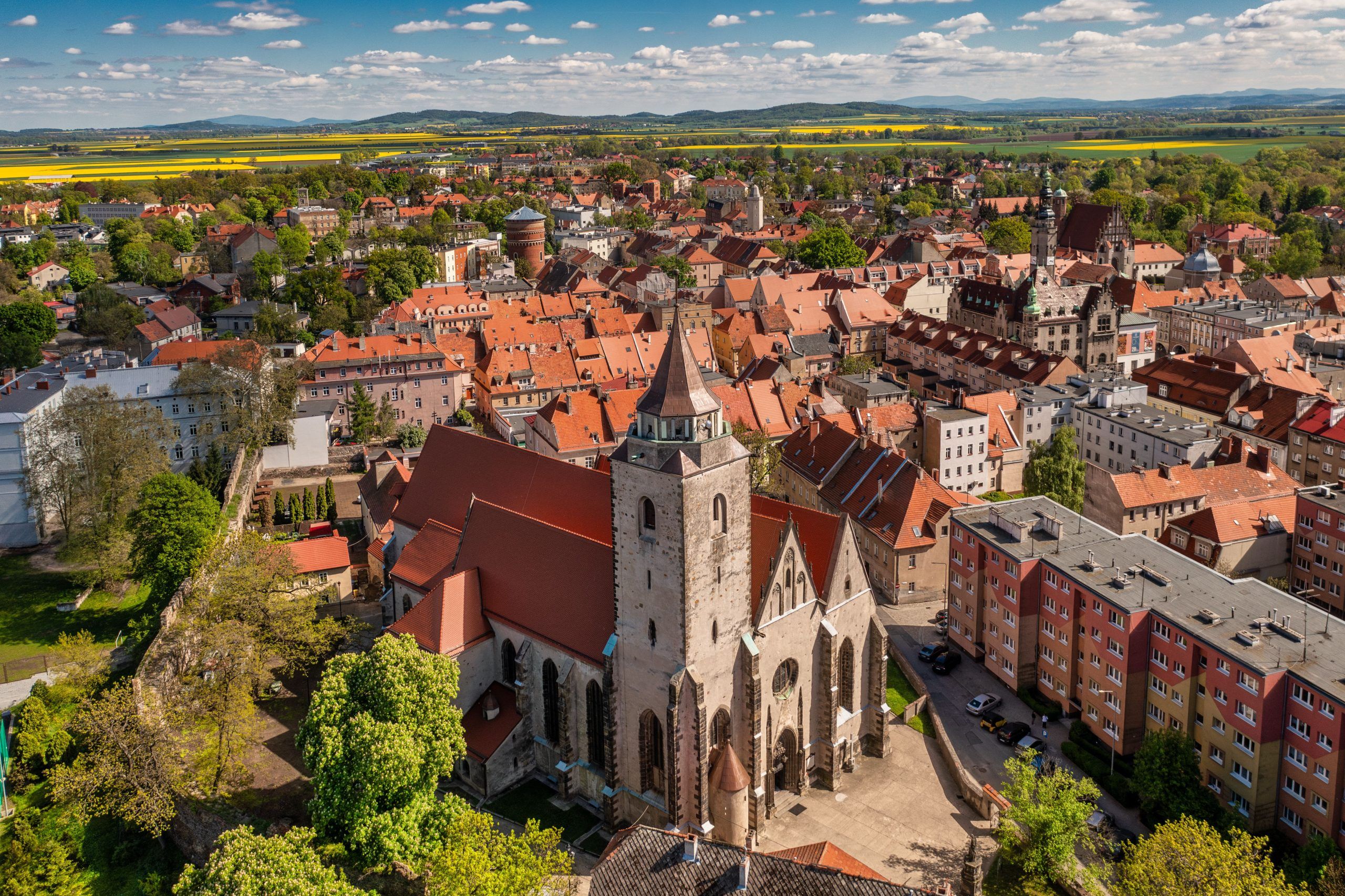 Monumentalna gotycka świątynia z wysoką wieżą i masywnymi, ceglastymi murami dominuje nad okoliczną zabudową.