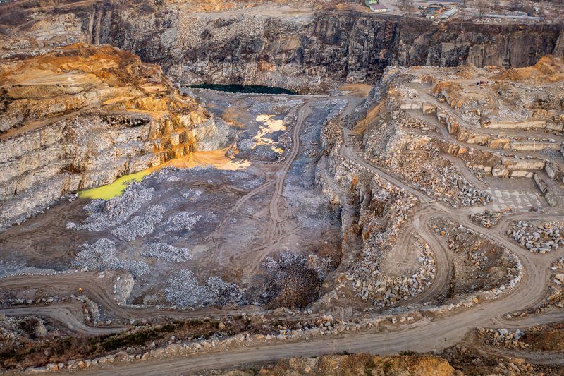 Na zdjęciu widać potężne, skalne ściany kamieniołomu w Strzelinie, z których wydobywa się granit, otoczone przez naturalną roślinność i malownicze jezioro w wykopach.