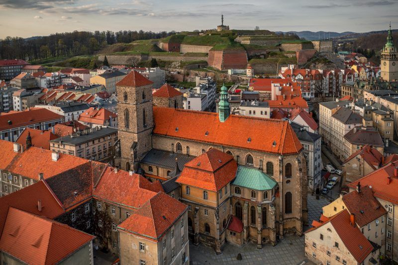 Gotycki kościół z czerwonej cegły i wysoką wieżą góruje nad gęstą zabudową kłodzkiej starówki.