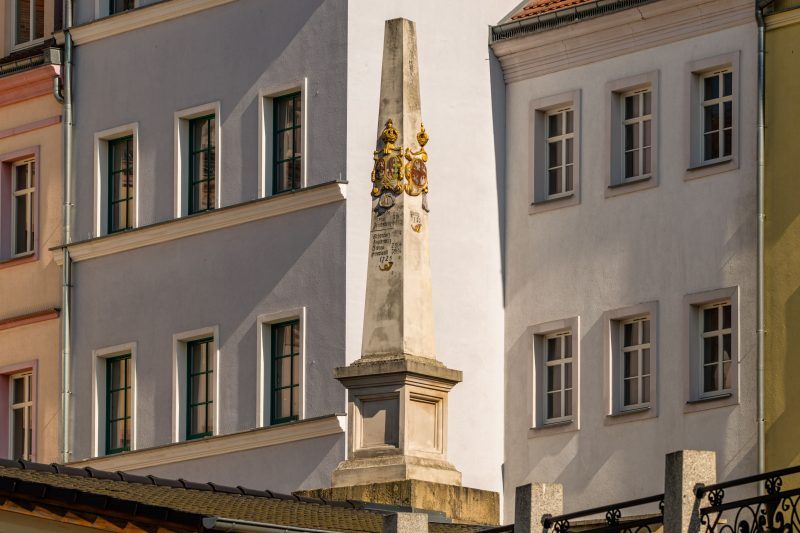 Kamienny, barokowy słup z herbami i inskrypcjami wskazującymi odległości do miast.