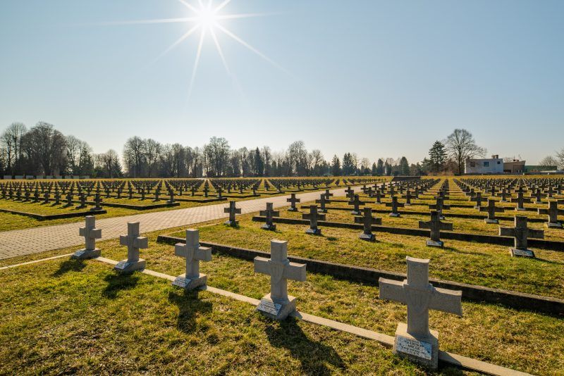 Na zdjęciu widać uporządkowany cmentarz z kamiennymi nagrobkami, otoczony zielenią, z zadbaną przestrzenią upamiętniającą żołnierzy II Armii Wojska Polskiego.