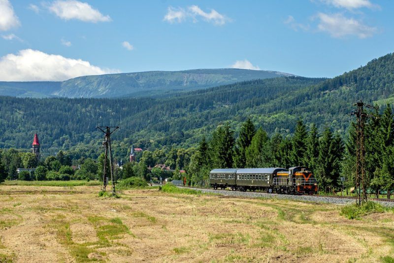 Widok z daleka na jadący pociąg oraz zazielenione góry w tle