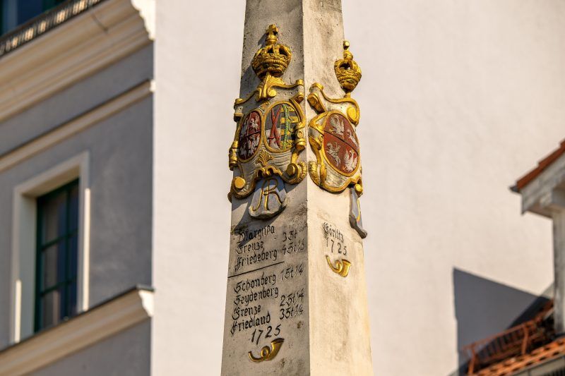 Kamienny, barokowy słup z herbami i inskrypcjami wskazującymi odległości do miast.