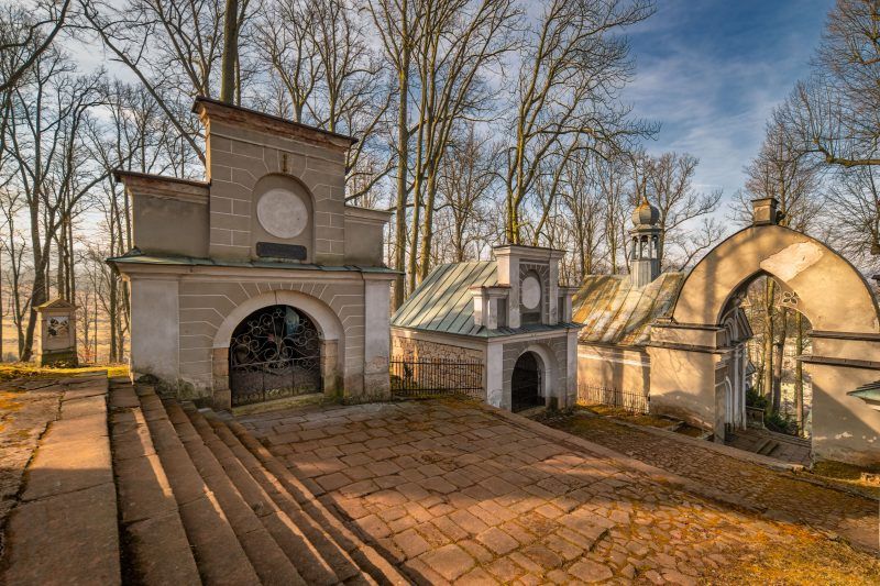 Na zdjęciu widać imponującą bazylikę w wznoszącą się na wzgórzu, otoczoną licznymi kapliczkami i zielenią, z monumentalnymi schodami prowadzącymi do jej bogato zdobionej fasady.