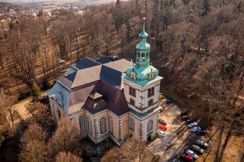 Na zdjęciu widać okazały Kościół Łaski w Kamiennej Górze – barokową budowlę o jasnej elewacji, wysokim dachu i smukłej wieży górującej nad otaczającym ją parkiem.