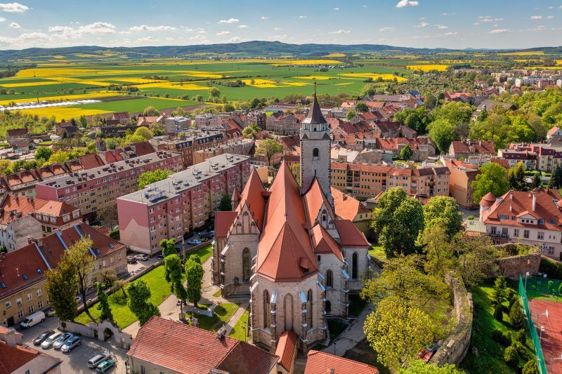 Monumentalna gotycka świątynia z wysoką wieżą i masywnymi, ceglastymi murami dominuje nad okoliczną zabudową.