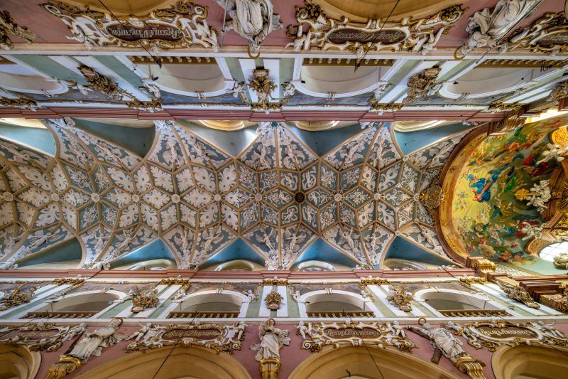 Wnętrze kościoła wypełniają wysokie, gotyckie sklepienia, smukłe filary i ciepłe światło przenikające przez witraże nad bogato zdobionymi ołtarzami.