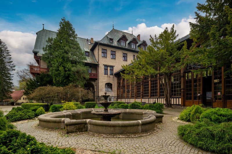 Na zdjęciu widać okazałą Halę Spacerową w Świeradowie-Zdroju – długą konstrukcję z drewnianymi zdobieniami, otoczoną zielenią i tętniącą uzdrowiskowym życiem.