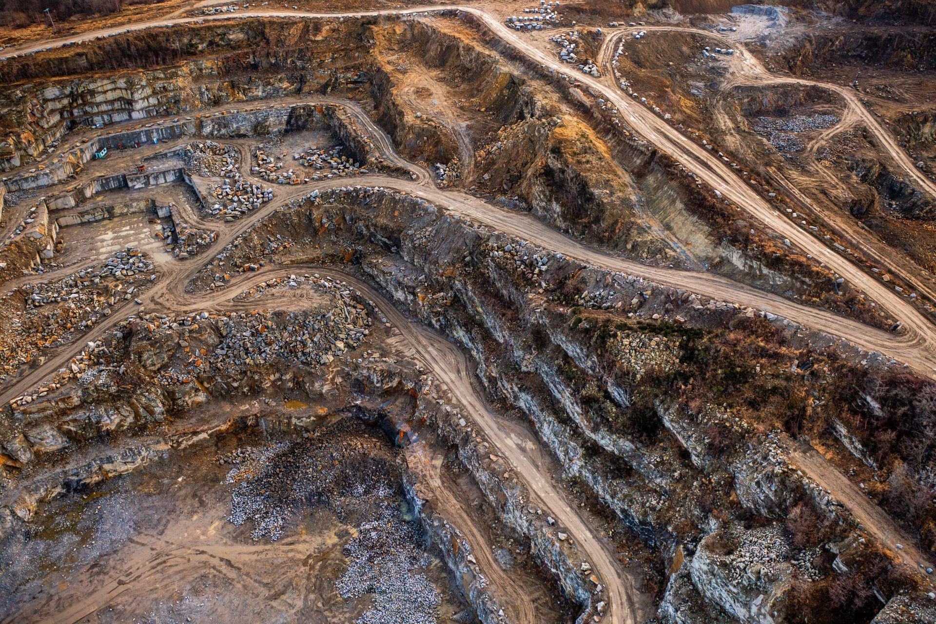 Na zdjęciu widać potężne, skalne ściany kamieniołomu w Strzelinie, z których wydobywa się granit, otoczone przez naturalną roślinność i malownicze jezioro w wykopach.