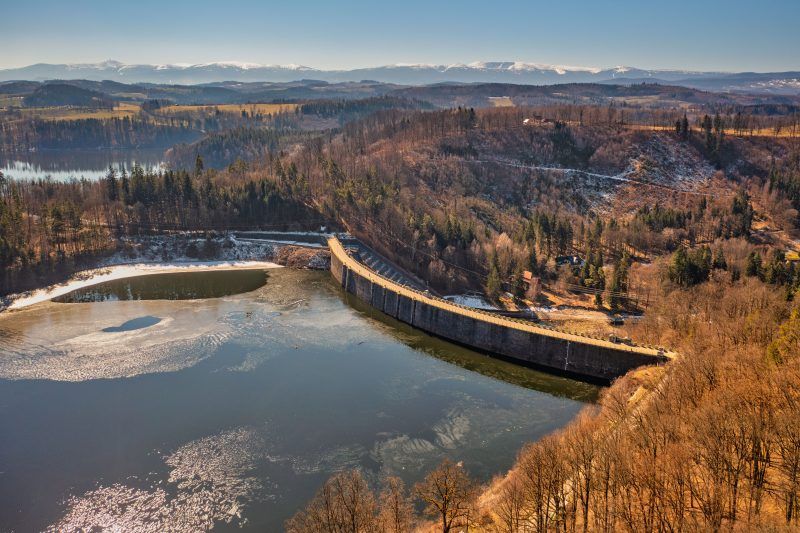 Na zdjęciu widać potężną kamienną zaporę w Pilchowicach, majestatycznie rozciągającą się wśród gór i odbijającą się w spokojnej tafli jeziora.