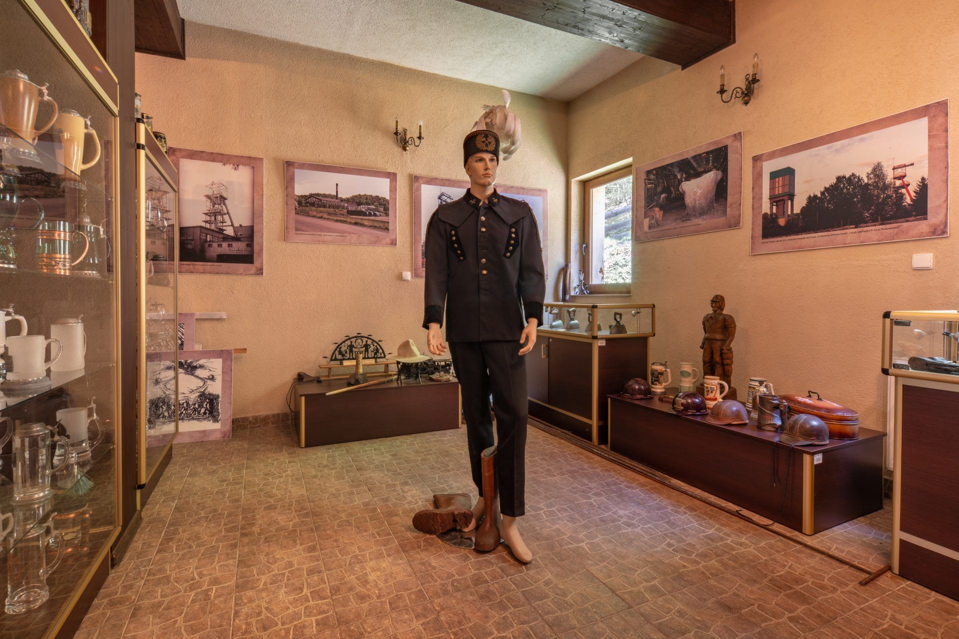 Wnętrze muzeum z manekinem ubranym w tradycyjny strój górniczy i eksponatami dotyczącymi historii górnictwa na ścianach i w gablotach.