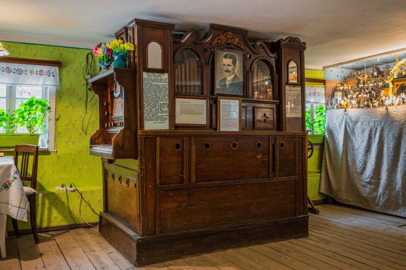 Na zdjęciu widać dużą, rzeźbioną drewnianą szafę z portretem twórcy, stojącą w zielonym, przytulnym wnętrzu Ruchomej Szopki.