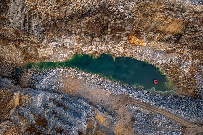 Na zdjęciu widać potężne, skalne ściany kamieniołomu w Strzelinie, z których wydobywa się granit, otoczone przez naturalną roślinność i malownicze jezioro w wykopach.