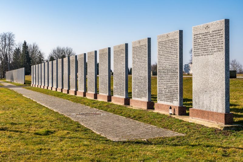 Na zdjęciu widać uporządkowany cmentarz z kamiennymi nagrobkami, otoczony zielenią, z zadbaną przestrzenią upamiętniającą żołnierzy II Armii Wojska Polskiego.