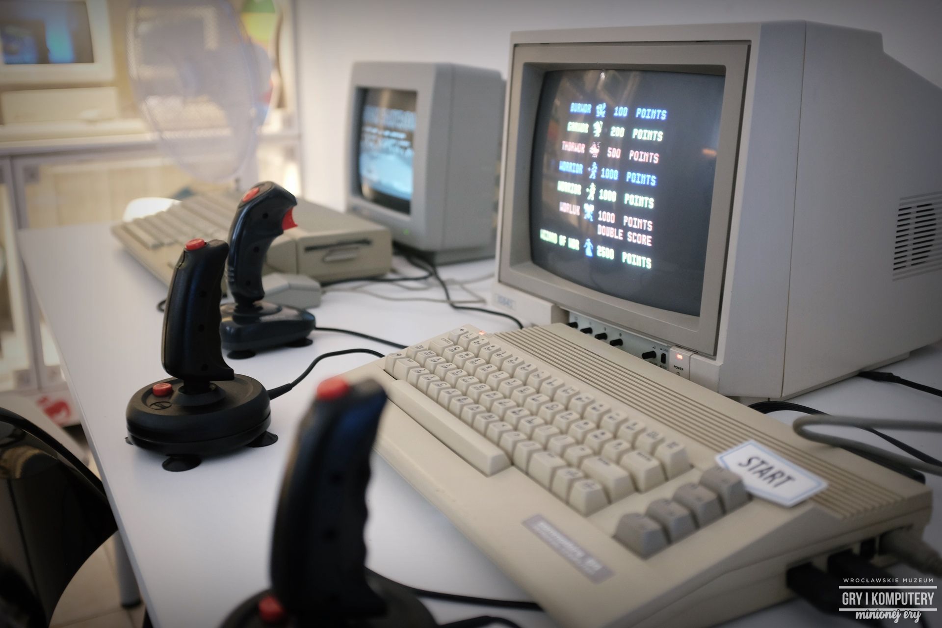 Dżojstiki i stare komputery leżące na stole w Muzeum Gier i Komputerów Minionej Ery