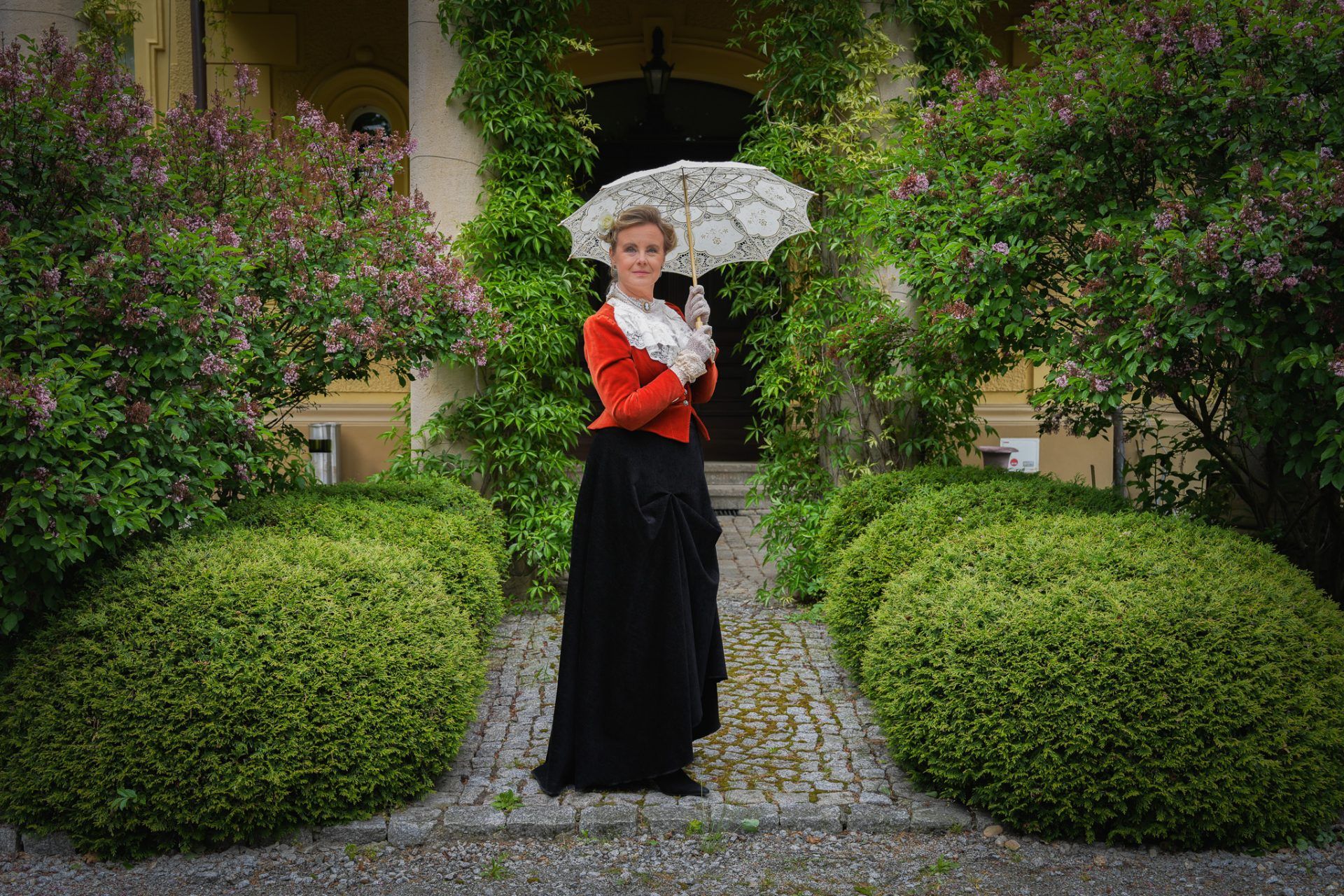 Kobieta w stroju z XIX wieku (rekonstrukcja) stoi na wprost wejścia do Pałacu Gruszów