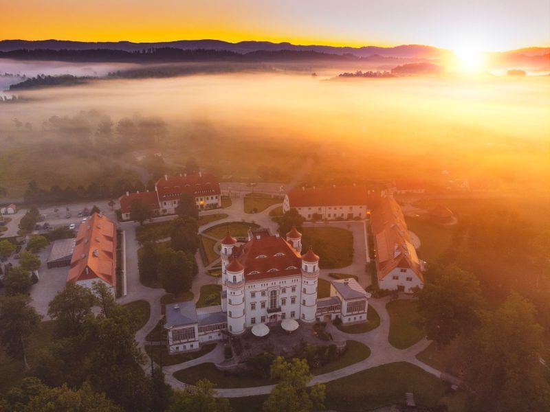 Widok z drona na spowity mgłą Pałac Wojanów na tle zachodzącego słońca
