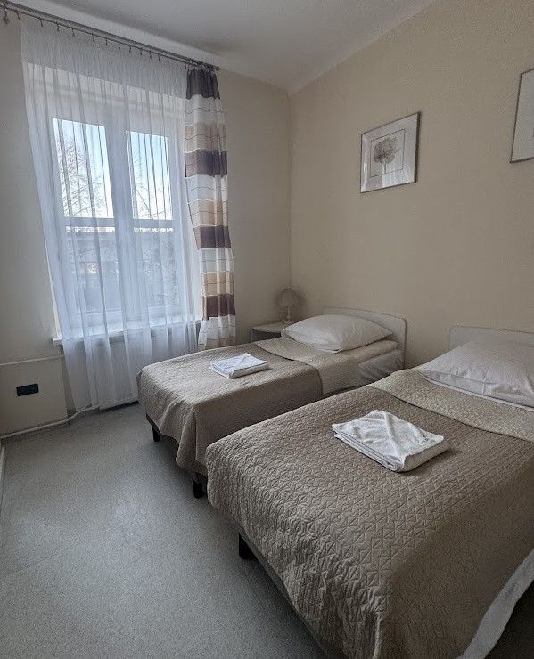 Pokój hotelowy urządzony w beżowych barwach z dwoma łóżkmai. 