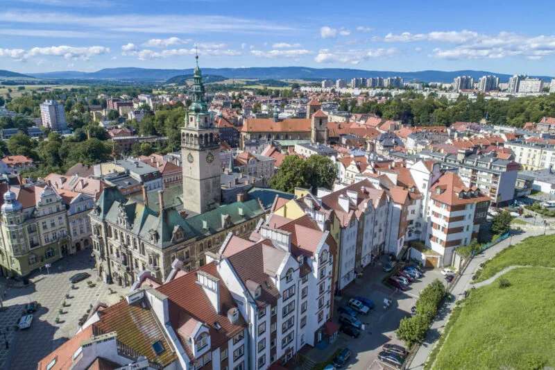 Widok ze szczytu góry na zabudowę Kłodzka z widocznymi szcytami gór w tle