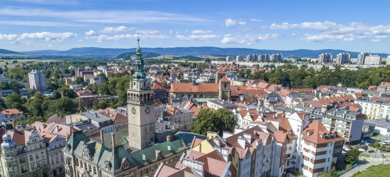 Widok ze szczytu góry na zabudowę Kłodzka z widocznymi szczytami gór w tle.