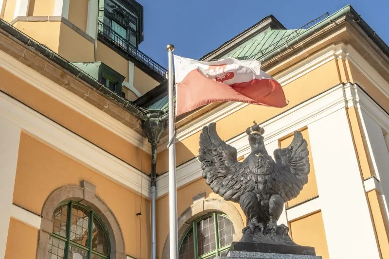 Metalowa rzeźba godła Polski z flagą Polski łopoczącą w tle na którym widać budynek kościoła w Jeleniej Górze
