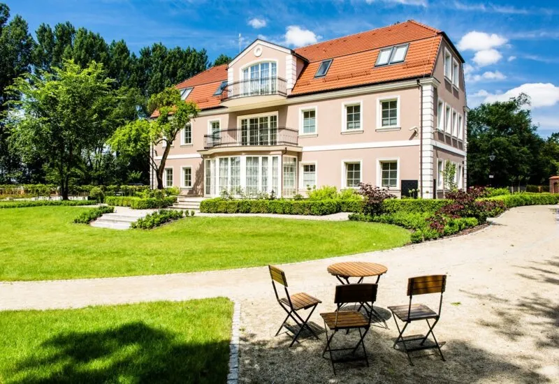 Zdjęcie przedstawia jedno z eleganckich budynków należących do kompleksu Zamku Topacz, otoczonego zadbanym ogrodem i miejscem do relaksu na świerzym powietrzu.