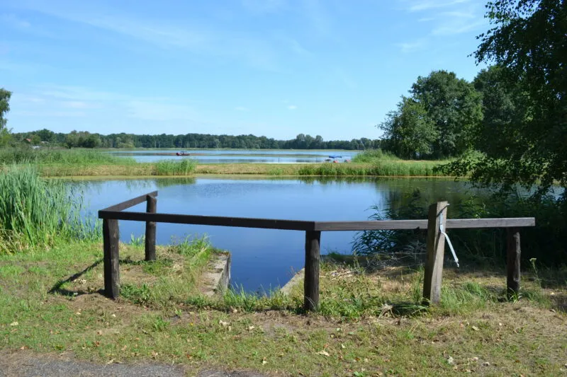 widok na jezioro w słoneczny dzień, na pierwszy planie znajdująsię drewanine słupki
