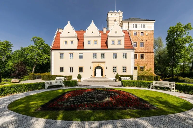 Główne wejście do zamku Topacz to imponująca brama z wieżą obronną, prowadząca na dziedziniec, otoczona murami i ozdobiona kamieniarskimi detalami.