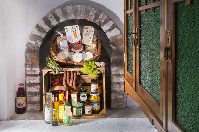 Przez otwarte okno w zabudowanej cegłami ścianie artystycznie ułożone produkty regionalne tworzące spójną wystawę z wielu różnych składników spożywczych.