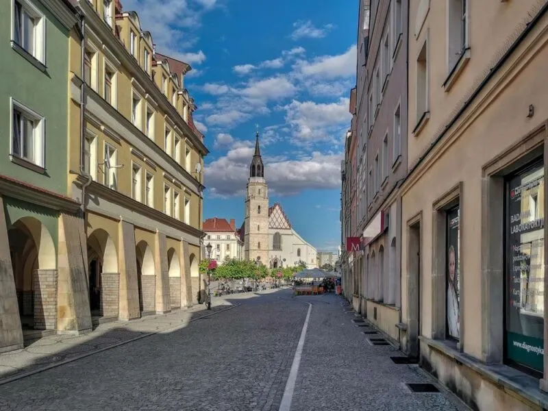 Widok na budynek z wysoką wieżą. Znajduje się na końcu ulicy, pomiędzy kamienicami.