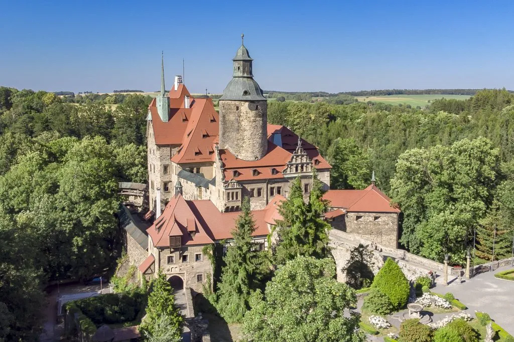 Widok z góry na dawny zamek z czerwonymi dachówkami, wieżą otoczony drzewami