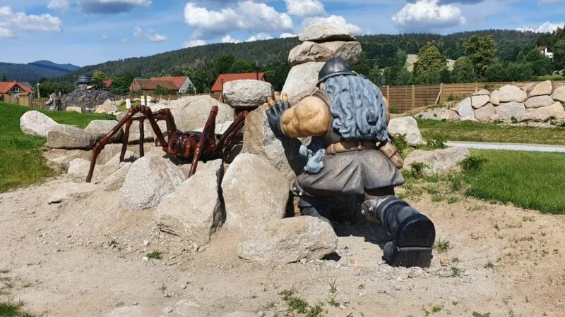 Spora figura pająka i dobrze zbudowanego mężczyzny wśród sterty głazów.