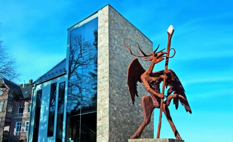 Davanti al moderno edificio di Karkonoskie Tajemnice si erge un'alta scultura dello Spirito della Montagna con le ali spiegate e un bastone luminoso.
