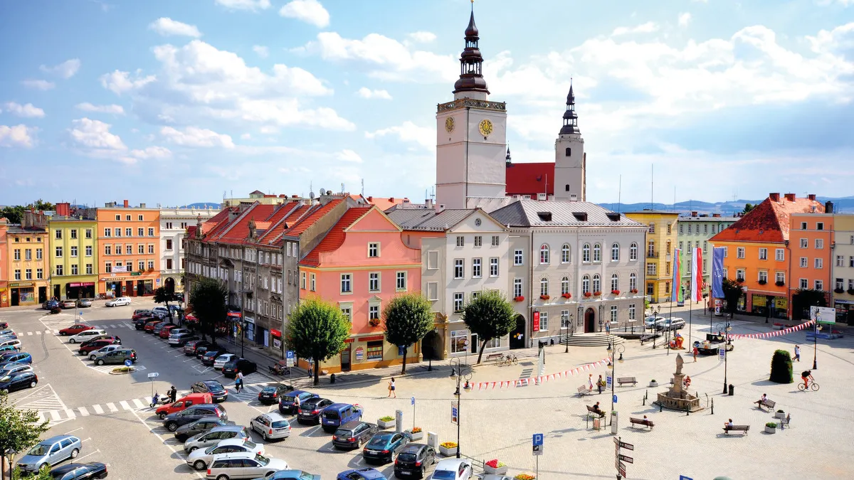 Widok na skąpany w słońcu rynek w Dzierżoniowie z widocznym blokiem śródrynkowym i masywną, kwadratową w swym planie wieżą ratuszową.