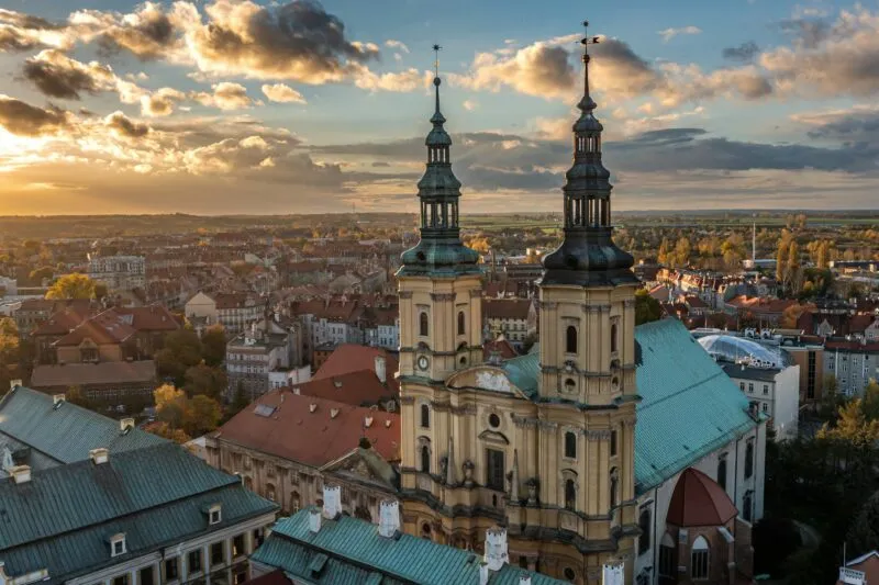 Kościół Świętego Jana i Mauzoleum Piastów w Legnicy z dwiema barokowymi wieżami góruje nad dachami miasta w świetle zachodzącego słońca.