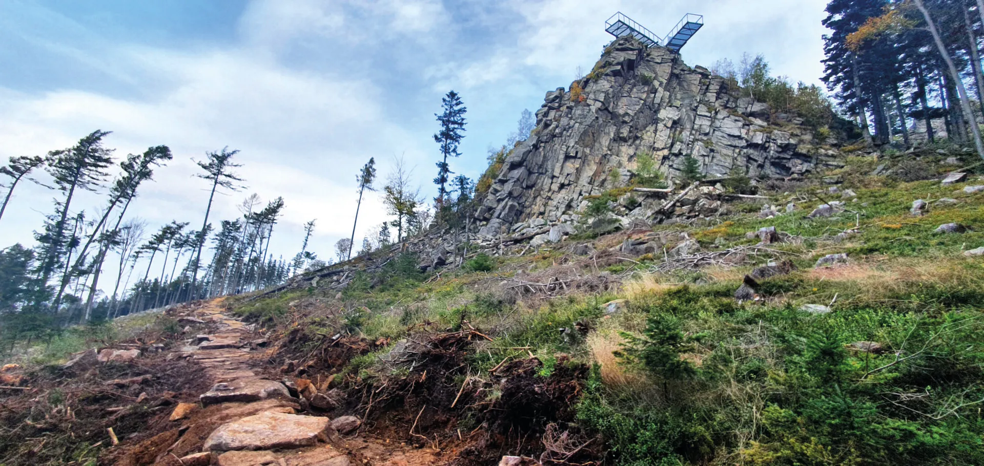 Widok na metalowy pomost-platformę od strony podejścia do wzniesienia. Platforma znajduje się na kamiennym ostańcu