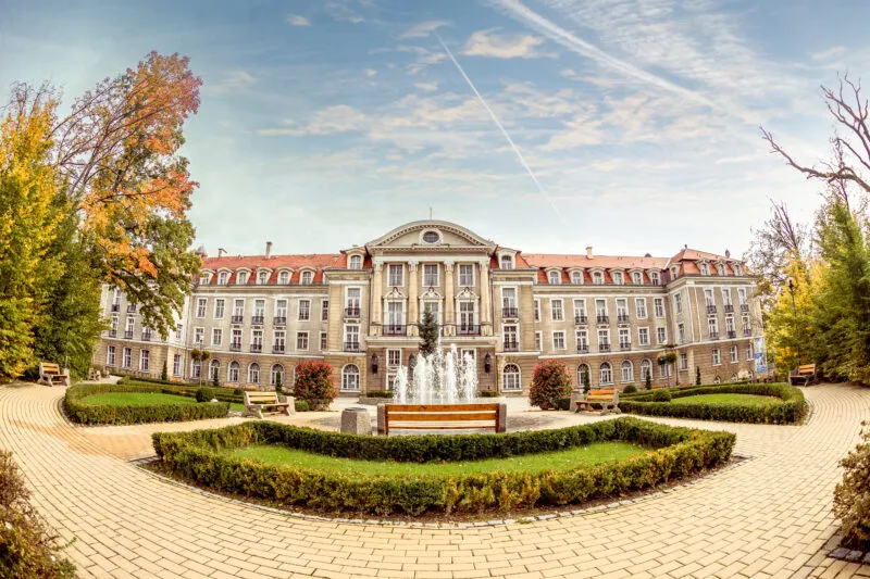 Szeroki, monumentalny, czterokondygnacyjny gmach Domu Zdrojowego, pokryty czerwoną dachówką.