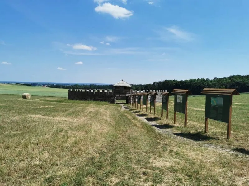Una fila di pannelli didattici conduce attraverso un terreno erboso a Obiszów fino a una palizzata di legno e alla torre di una replica di un castello medievale.