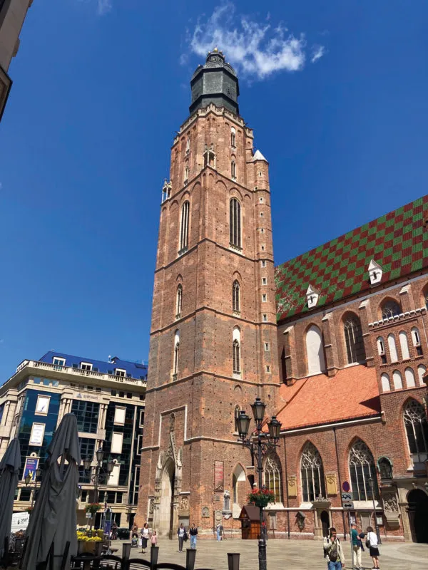 Widok z poziomu ulicy na oświetloną promieniami słońca ceglaną, prawie 100-metrową, kwadratową w swym planie wieżę kościoła farnego św. Elżbiety we Wrocławiu