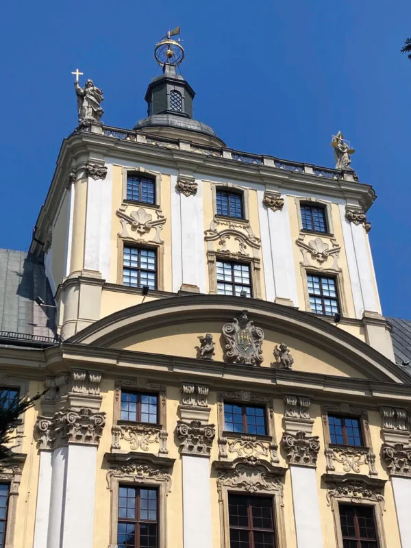 Widok z poziomu ulicy na szczyt barokowej, około 60-metrowej wieży z niezadaszonym tarasem widokowym z alegoriami 4 pierwszy fakultetów uniwersytetu na balustradzie.