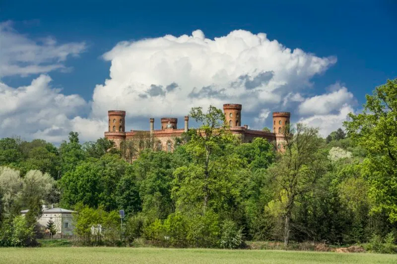 Il Palazzo di Marianna d'Orange a Kamieniec Ząbkowicki, con le sue quattro torri di mattoni, si erge sopra il parco verde sotto alte nuvole bianche.