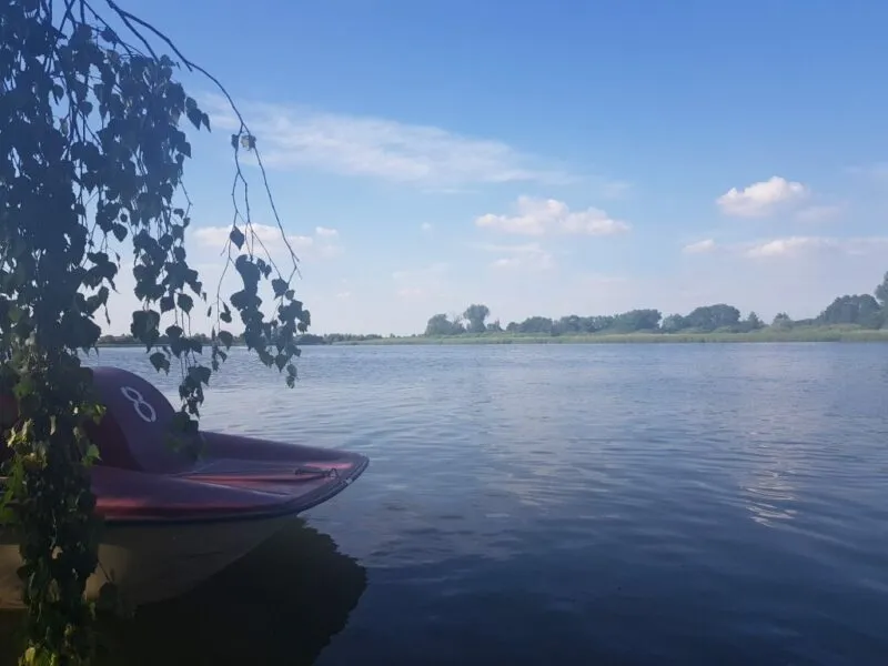 Jezioro z łódką przy brzegu, w oddali brzeg z drzewami