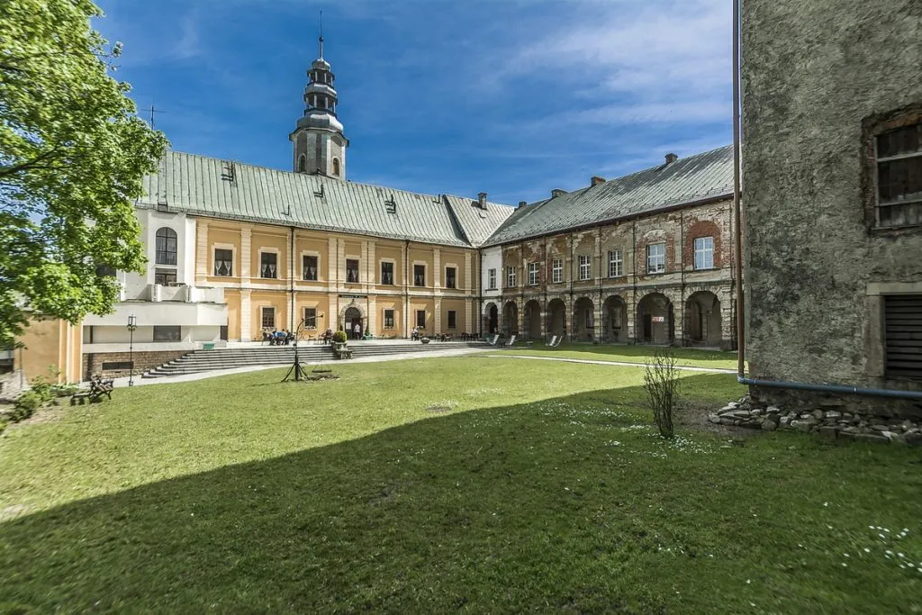 Na pierwszym planie zielona trawa, widoczna część zamku z nową elewacją, żółtą z białymi akcentami. Widać część zamku nieodrestaurowana.
